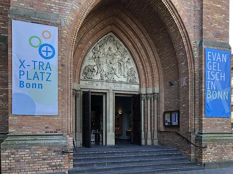 Kircheneingang mit Bannern für „X-TRA PLATZ“ und „Evangelisch in Bonn“.
