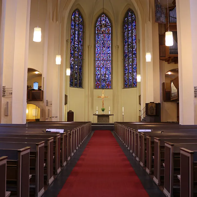 Leere Kirchenbänke, roter Teppich und Blick auf den Altar.