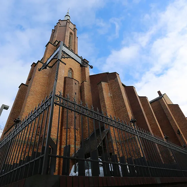 Backsteinkirche aus Froschperspektive hinter einem Metallzaun.