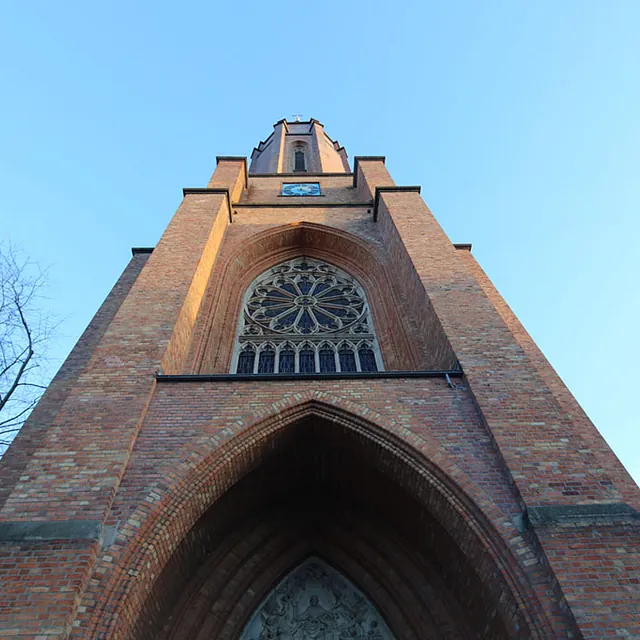 Hoher Backsteinkirchturm in der Untersicht vor blauem Himmel.