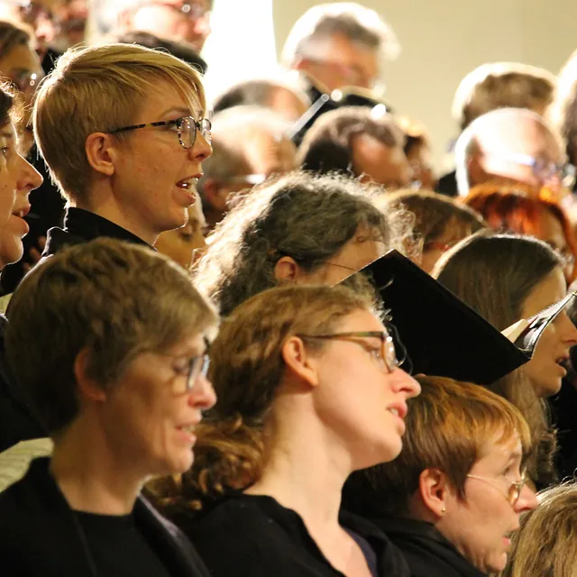 Eine Nahaufnahme von Chormitgliedern in der Seitenansicht, die während eines Auftritts konzentriert und emotional singen.