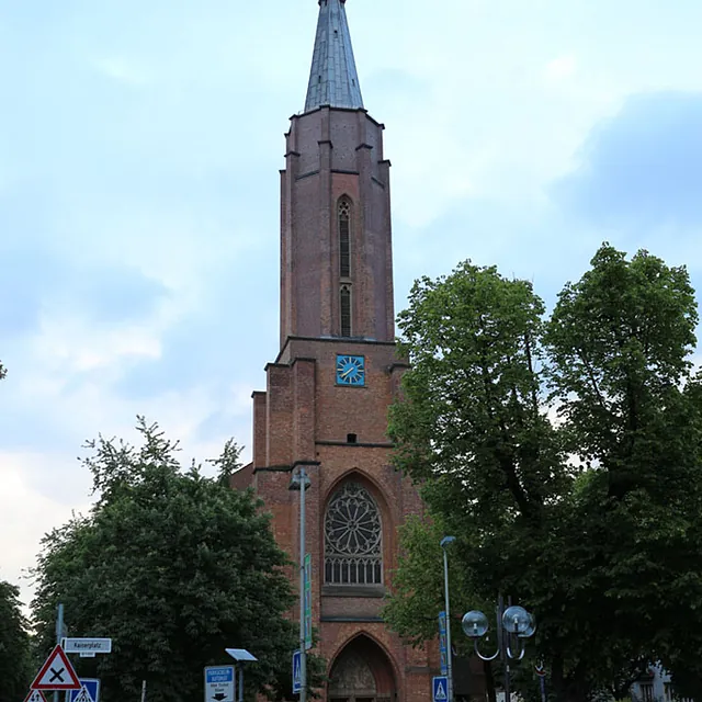 Hohe Backsteinkirche von einem Platz mit Springbrunnen aus gesehen.