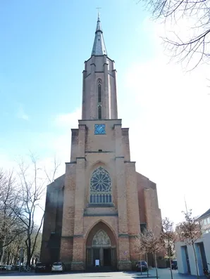Hohe Backsteinkirche mit spitzem Turm und blauem Zifferblatt.